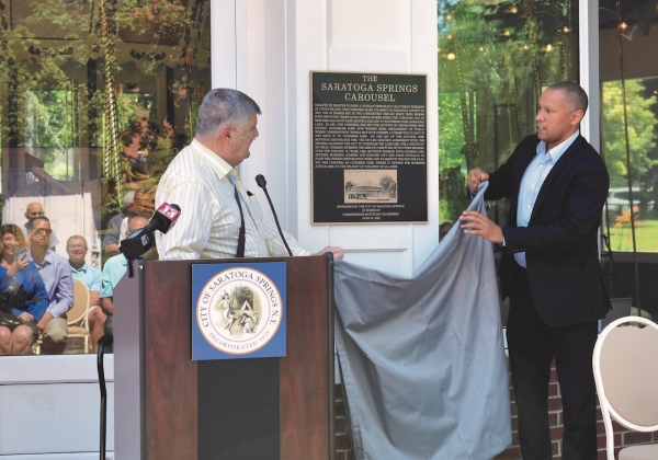 Former Saratoga Springs DPW Commissioner Tom McTygue, at left, and current Commissioner Jason Golub, unveil a plaque in Congress Park on June 29, 2022, detailing the history of the carousel and commemorating the leadership of McTygue. Photo by SuperSource Media.  